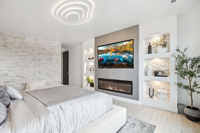 bedroom featuring a glass covered fireplace and wood finished floors