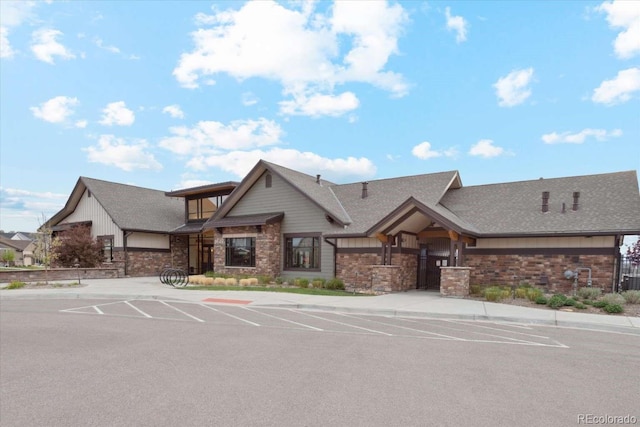view of front of property featuring stone siding, uncovered parking, and roof with shingles