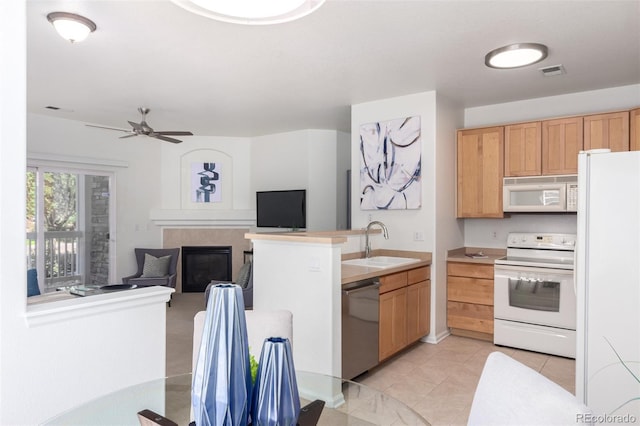 kitchen with white appliances, ceiling fan, sink, a tile fireplace, and light tile patterned floors