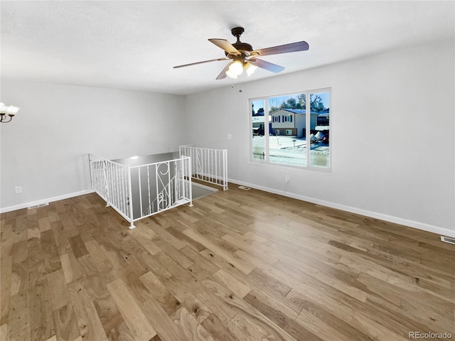 empty room with ceiling fan with notable chandelier and hardwood / wood-style floors