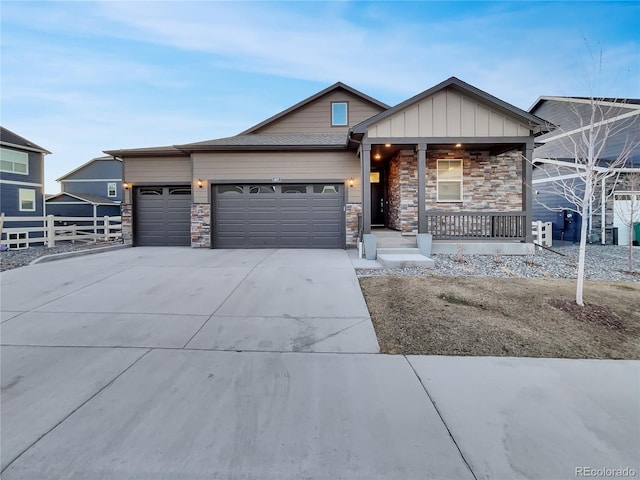 view of front of home with covered porch, concrete driveway, an attached garage, board and batten siding, and stone siding