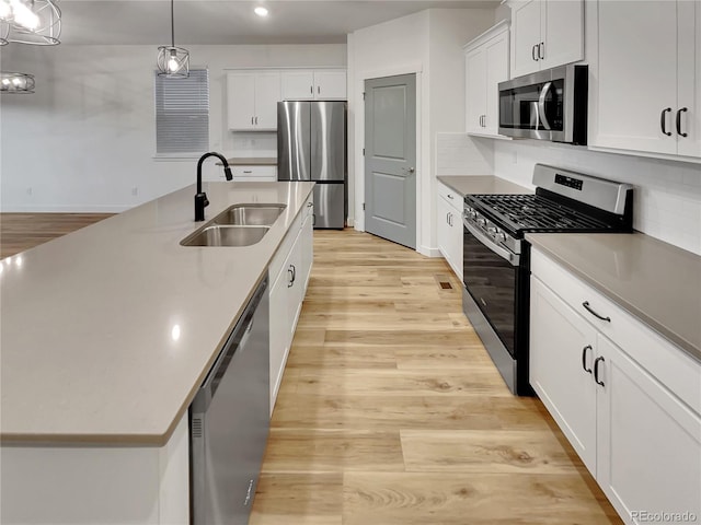 kitchen featuring appliances with stainless steel finishes, a sink, light wood-style flooring, and tasteful backsplash