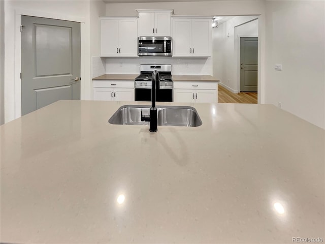 kitchen featuring light wood finished floors, white cabinets, stainless steel appliances, light countertops, and a sink