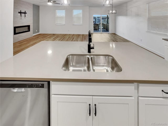 kitchen with a large fireplace, wood finished floors, a sink, white cabinetry, and stainless steel dishwasher