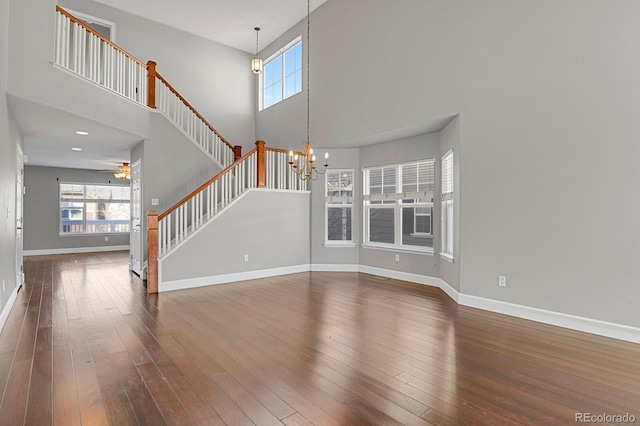 unfurnished living room featuring ceiling fan with notable chandelier, a towering ceiling, and dark hardwood / wood-style flooring