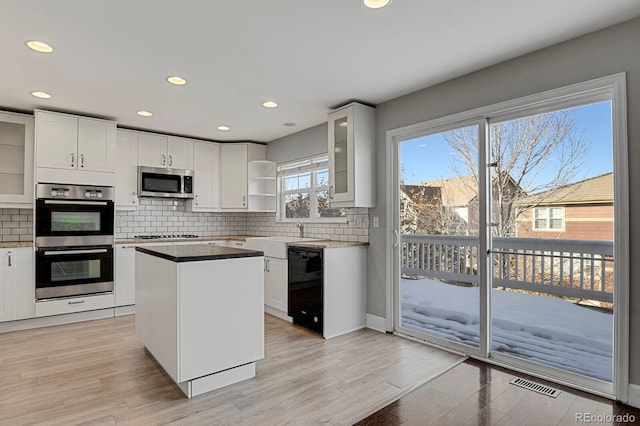 kitchen with stainless steel appliances, sink, white cabinetry, light hardwood / wood-style flooring, and a kitchen island