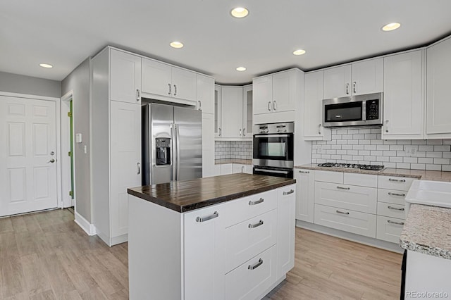 kitchen with white cabinets, light wood-type flooring, stainless steel appliances, and tasteful backsplash