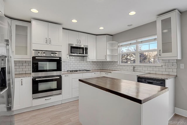 kitchen featuring white cabinets, sink, light wood-type flooring, appliances with stainless steel finishes, and tasteful backsplash