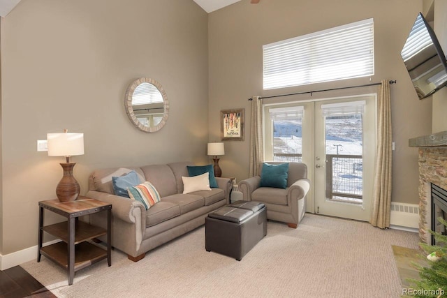 living area featuring french doors, a fireplace, light colored carpet, a high ceiling, and baseboards