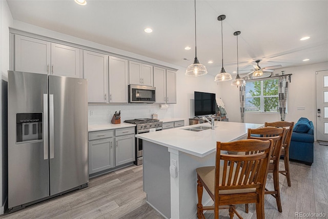 kitchen featuring open floor plan, gray cabinets, a sink, light wood-style flooring, and stainless steel appliances