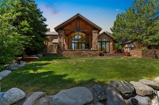 back of house at dusk featuring a lawn, stone siding, and french doors