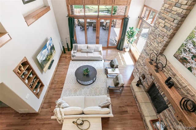 living area featuring a tiled fireplace, a towering ceiling, and wood finished floors