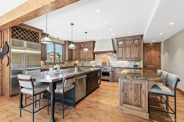 kitchen featuring high end appliances, premium range hood, a large island with sink, and a sink