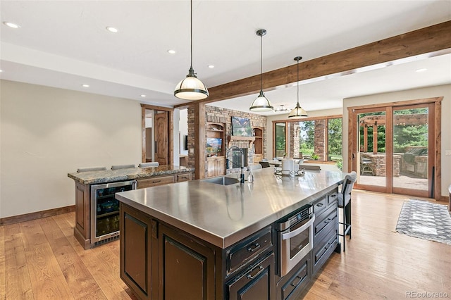 kitchen with a spacious island, stainless steel countertops, wine cooler, light wood-style flooring, and a sink