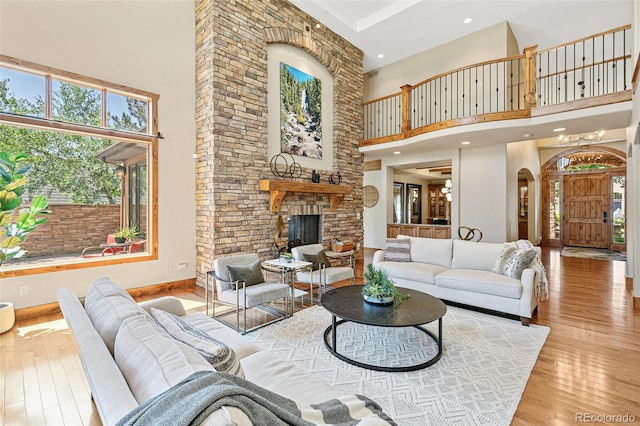 living area featuring baseboards, hardwood / wood-style floors, recessed lighting, a fireplace, and a high ceiling