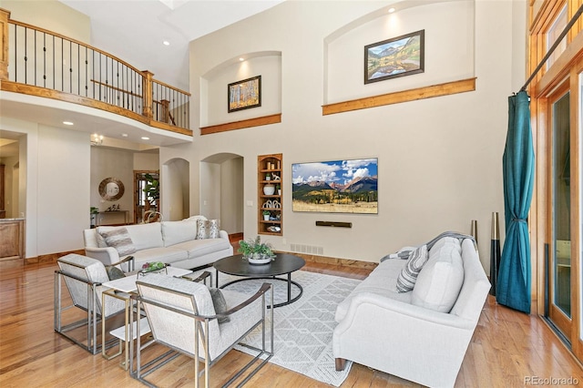 living area featuring visible vents, built in shelves, wood finished floors, arched walkways, and a high ceiling