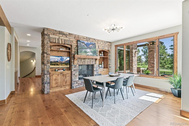 dining area featuring a fireplace, arched walkways, wood-type flooring, and baseboards