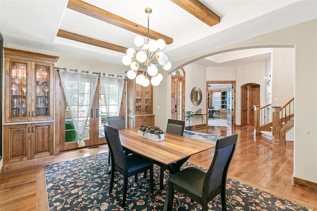 dining room featuring stairs, beam ceiling, light wood-style floors, arched walkways, and a notable chandelier