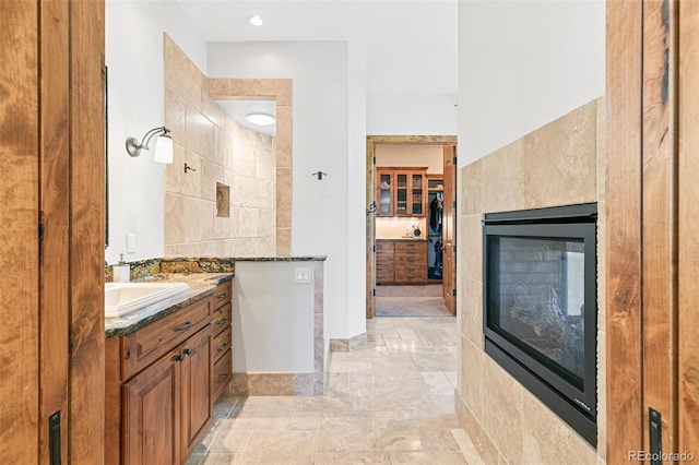 full bath with a multi sided fireplace, stone tile flooring, and vanity