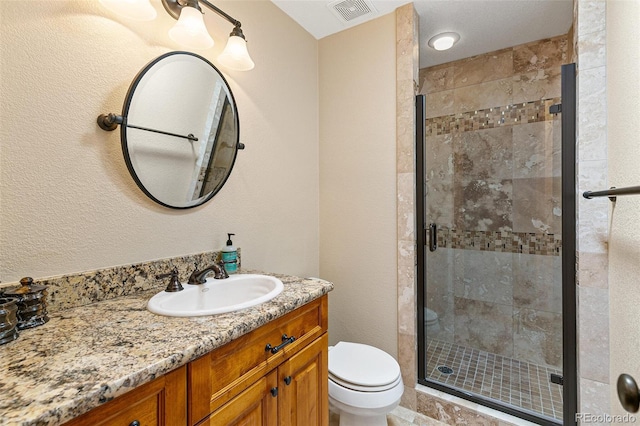 bathroom with vanity, a shower stall, toilet, and visible vents