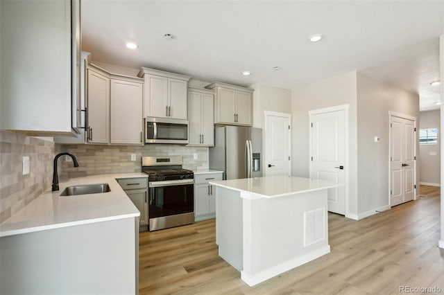 kitchen with light wood finished floors, a sink, light countertops, tasteful backsplash, and appliances with stainless steel finishes