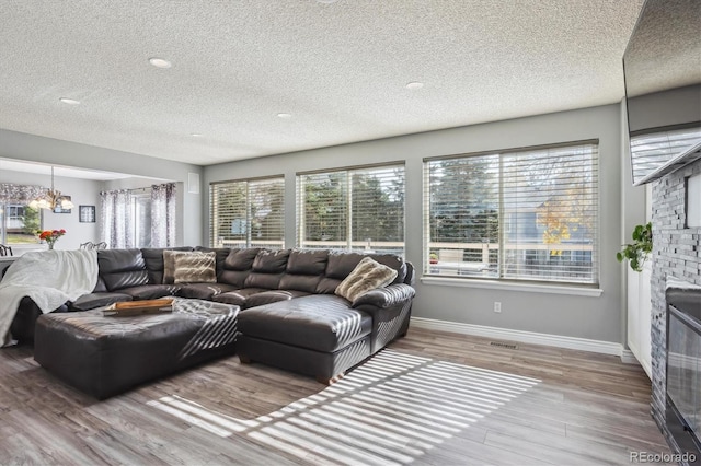 living room featuring a stone fireplace, a textured ceiling, and hardwood / wood-style flooring