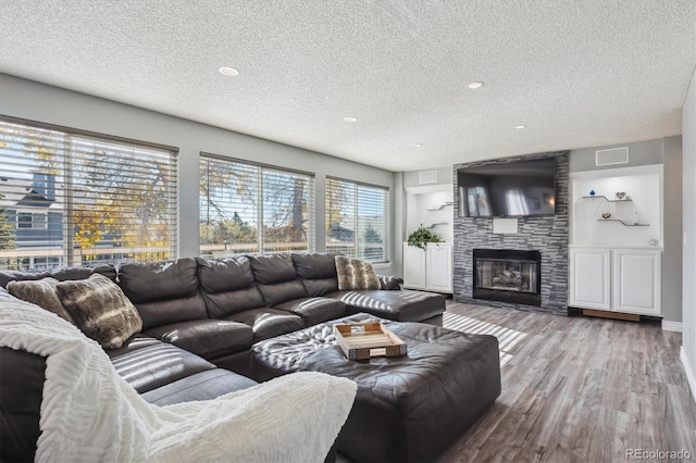 living room featuring wood-type flooring, a textured ceiling, plenty of natural light, and a fireplace