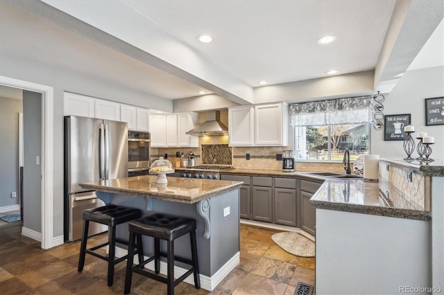 kitchen with appliances with stainless steel finishes, sink, wall chimney exhaust hood, white cabinets, and a breakfast bar