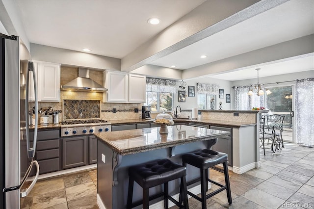 kitchen featuring appliances with stainless steel finishes, kitchen peninsula, a kitchen breakfast bar, wall chimney exhaust hood, and white cabinets