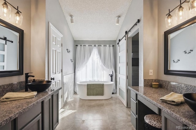 bathroom with a textured ceiling, tile patterned floors, lofted ceiling, a bathing tub, and vanity