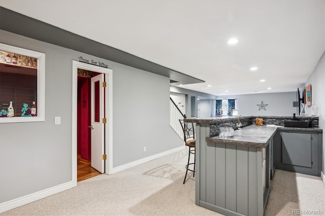 kitchen featuring gray cabinets, kitchen peninsula, light colored carpet, and a kitchen breakfast bar