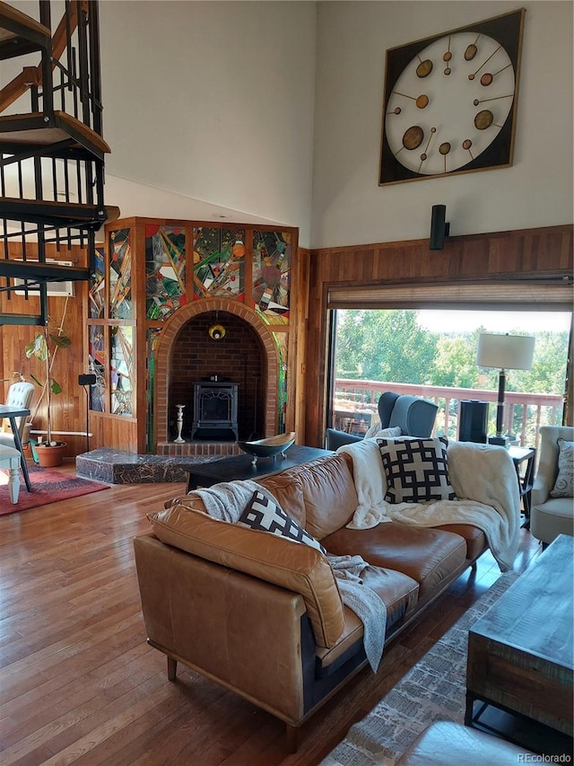 living room with hardwood / wood-style flooring, wooden walls, a wood stove, and a high ceiling