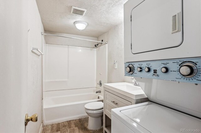 full bathroom with stacked washer / drying machine, toilet, a textured ceiling, vanity, and hardwood / wood-style floors