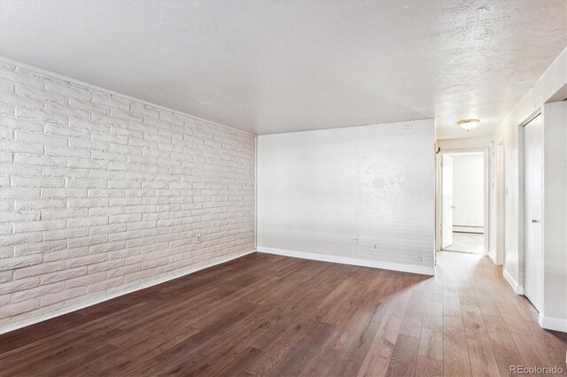 unfurnished room featuring hardwood / wood-style flooring, brick wall, and a textured ceiling