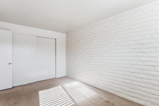 unfurnished bedroom with light colored carpet, brick wall, and a closet