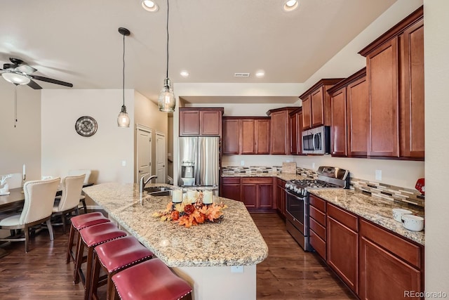 kitchen featuring a center island with sink, appliances with stainless steel finishes, a breakfast bar, dark hardwood / wood-style floors, and pendant lighting