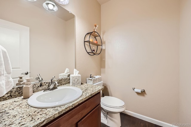 half bathroom featuring toilet, vanity, baseboards, and wood finished floors