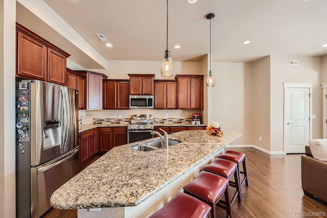 kitchen with dark hardwood / wood-style floors, a breakfast bar area, stainless steel appliances, a center island with sink, and decorative light fixtures