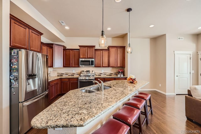 kitchen with appliances with stainless steel finishes, sink, a kitchen bar, hanging light fixtures, and a kitchen island with sink