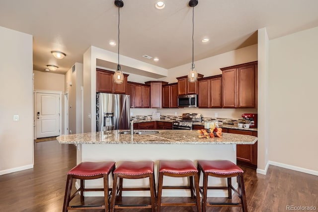 kitchen featuring dark wood-type flooring, a breakfast bar, a sink, stainless steel appliances, and baseboards