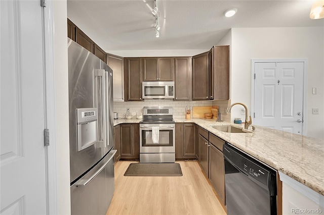 kitchen featuring rail lighting, light stone counters, stainless steel appliances, sink, and light hardwood / wood-style flooring