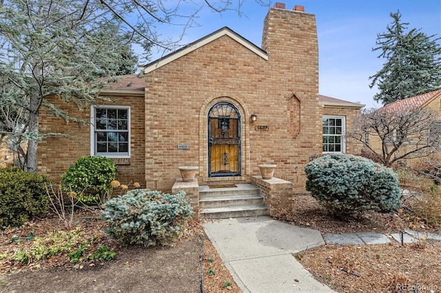 view of front of house featuring roof with shingles, a chimney, and brick siding