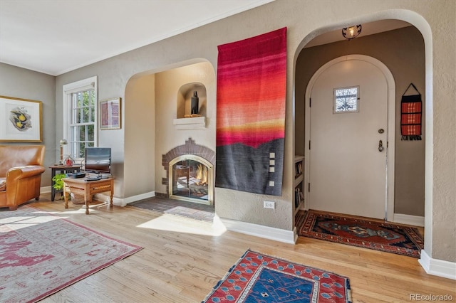 foyer featuring arched walkways, ornamental molding, wood finished floors, a warm lit fireplace, and baseboards