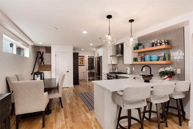 kitchen featuring a sink, appliances with stainless steel finishes, a breakfast bar area, and wall chimney range hood