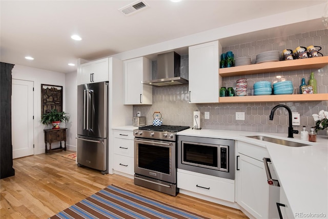 kitchen featuring visible vents, a sink, open shelves, appliances with stainless steel finishes, and wall chimney range hood