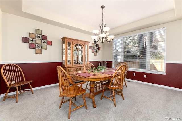 dining room with a raised ceiling, light carpet, a notable chandelier, and baseboards