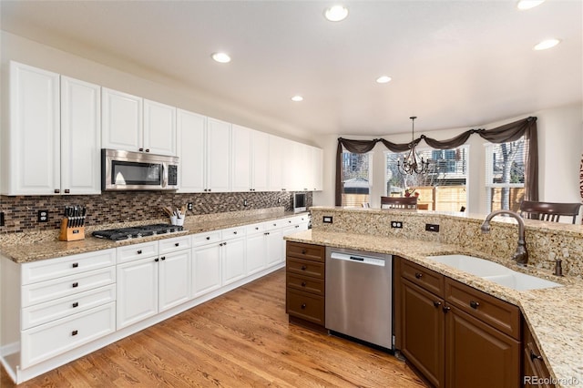 kitchen with light wood finished floors, tasteful backsplash, appliances with stainless steel finishes, white cabinetry, and a sink