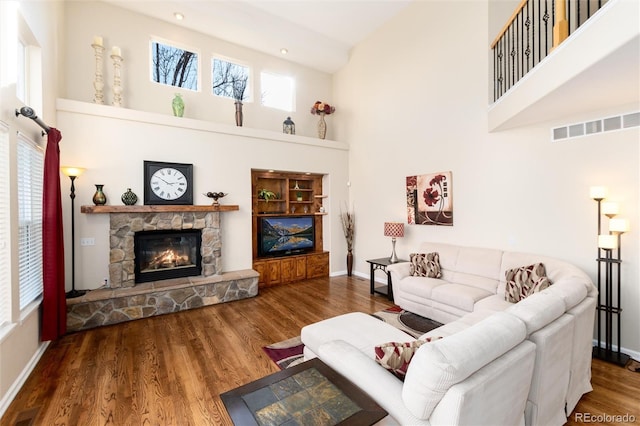 living area featuring visible vents, a fireplace, a high ceiling, and wood finished floors