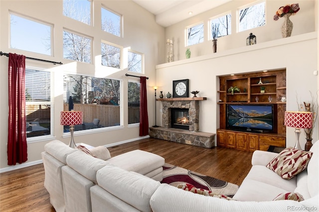 living area featuring a high ceiling, baseboards, wood finished floors, and a stone fireplace