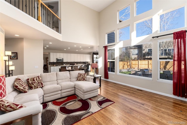 living room featuring a high ceiling, light wood-type flooring, recessed lighting, and baseboards